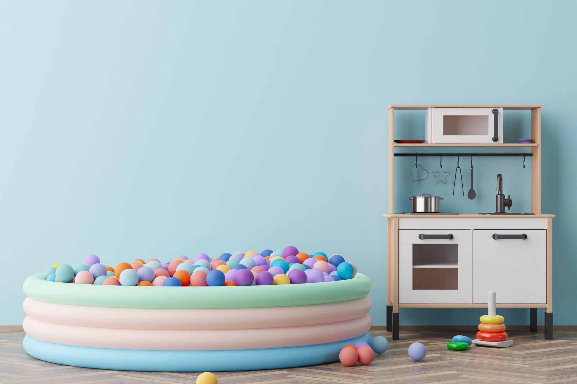 Vibrant children's playroom featuring a colorful ball pit, a wooden kitchen playset, and assorted toys on a sleek wooden floor, set against a soft blue wall with ample space. 3D render.