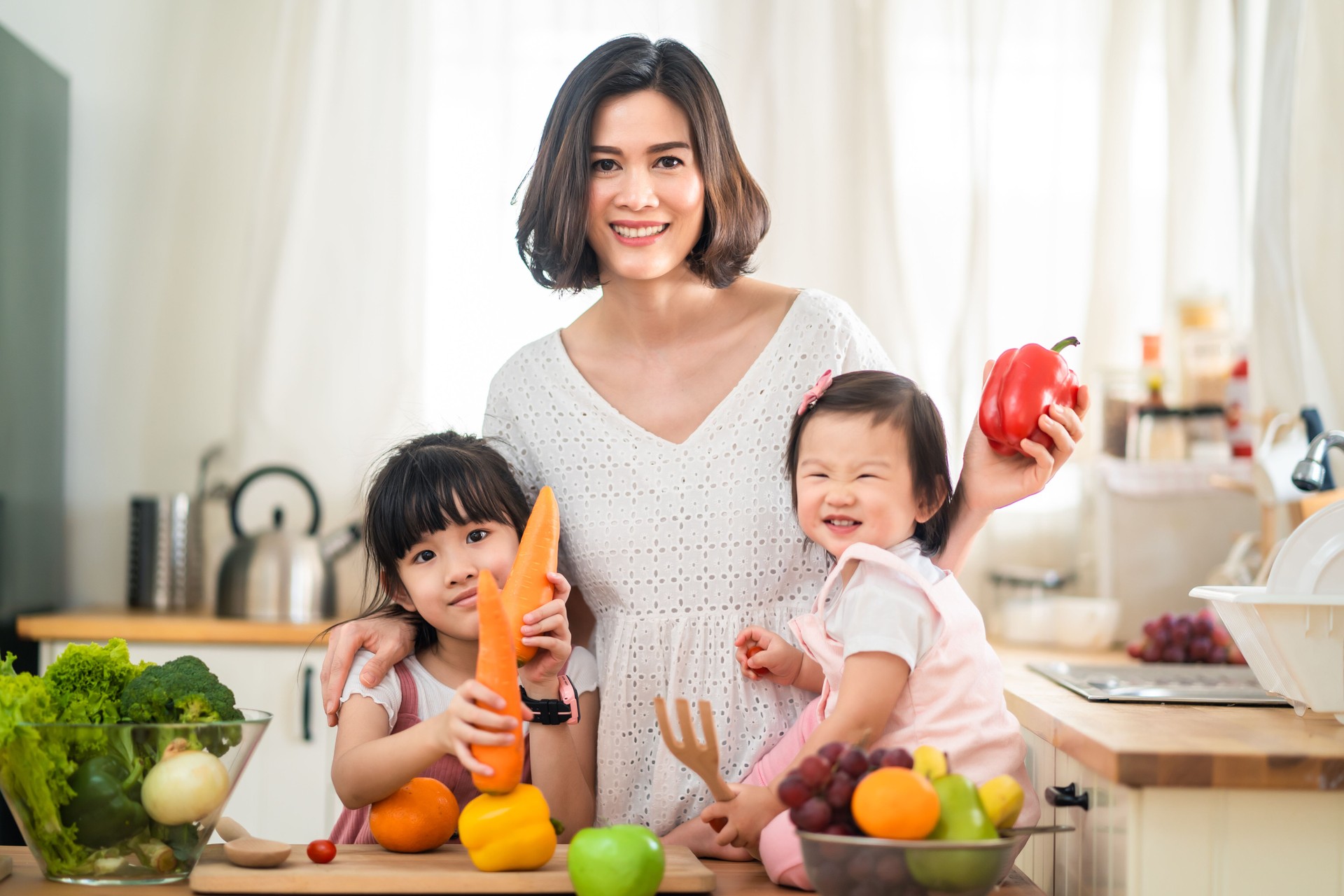 Lovely cute Asian family playing, making food in kitchen at home. Portrait of smiling mother and children standing at cooking counter that food ingredient put on table. Happy family activity together.